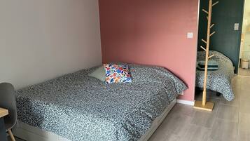 Un lit simple avec une couvre-lit à motifs floraux, un mur d’accent rouge et un porte-manteau en bois.