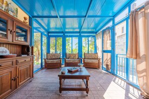 Une pièce baignée de lumière, avec un plafond bleu, des meubles en bois et une vue dégagée sur l’extérieur grâce à de grandes fenêtres.