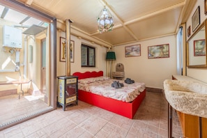 Une chambre à coucher avec un lit rouge, une armoire en bois, un lustre et une grande fenêtre.