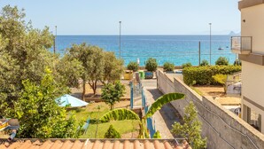 Une vue sur la côte, avec un ciel dégagé, une mer et un bâtiment doté d’un balcon donnant sur la mer.