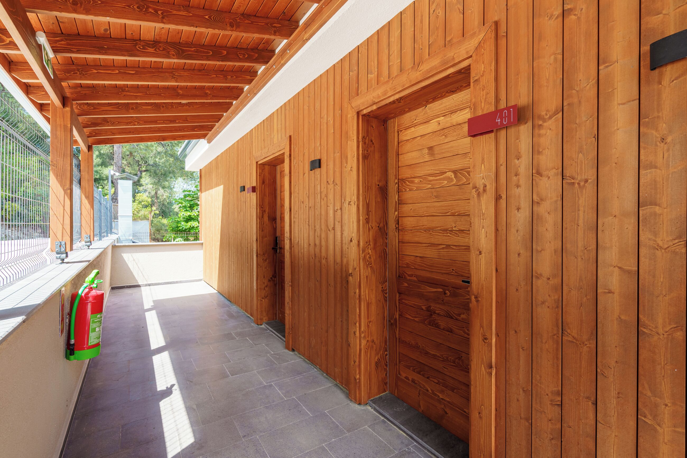 Un corridoio con pareti e porte in legno, un estintore e un balcone con ringhiera metallica.