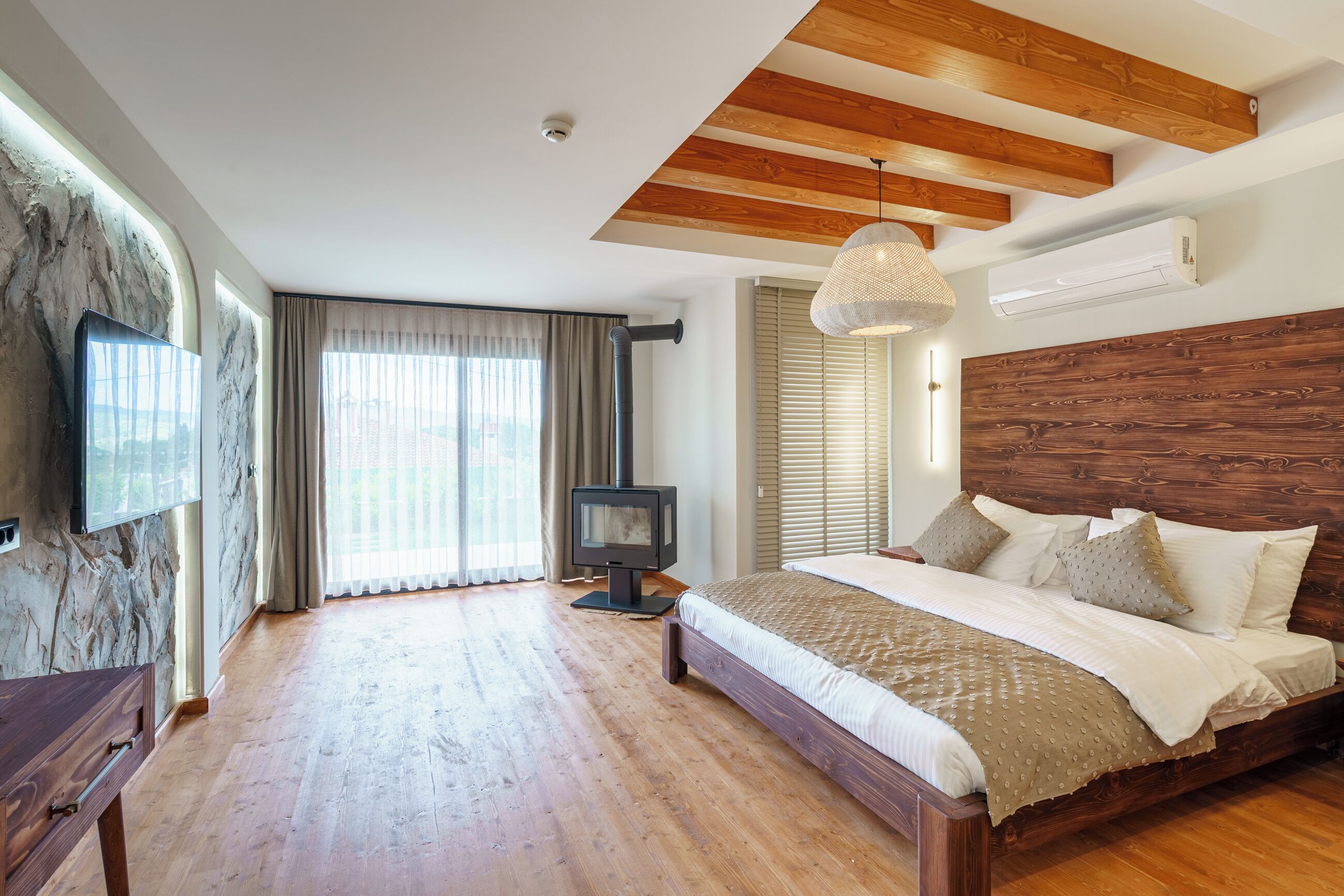 Een slaapkamer met een houten plafond, een groot bed, een televisie en een open haard.