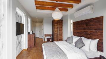Un dormitorio con cabecera de madera, cama grande con ropa de cama gris, lámpara colgante y armario de madera.