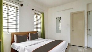 A bedroom with a bed, a window with blinds, a door, and a light fixture on the wall. - S M Suites (Bengaluru)
