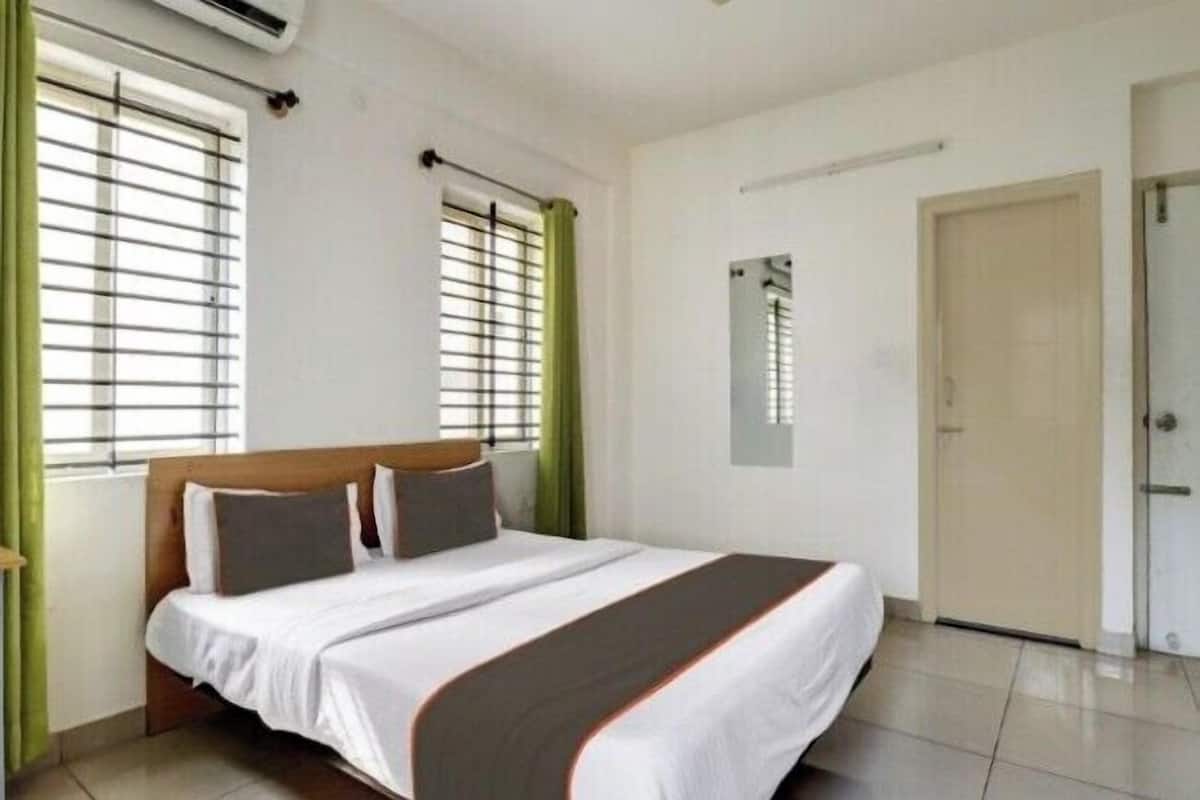 Une chambre à coucher avec un lit, une fenêtre avec des stores, une porte et un luminaire fixé au mur.