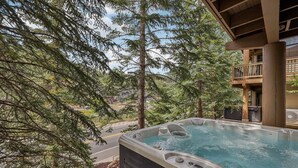 Ein Whirlpool mit Blick auf einen Wald und ein Gebäude mit einem Balkon.