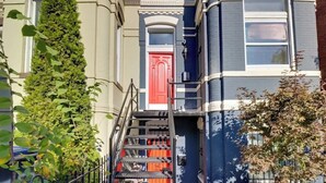 Un immeuble à plusieurs étages avec une porte rouge, un escalier et un arbre devant.