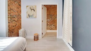 Une chambre avec un mur en briques, un lit, un radiateur et une porte donnant sur une autre pièce.
