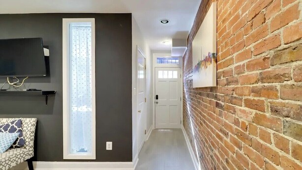 Un couloir avec un mur sombre, une porte blanche et un mur de briques orné d’un tableau.