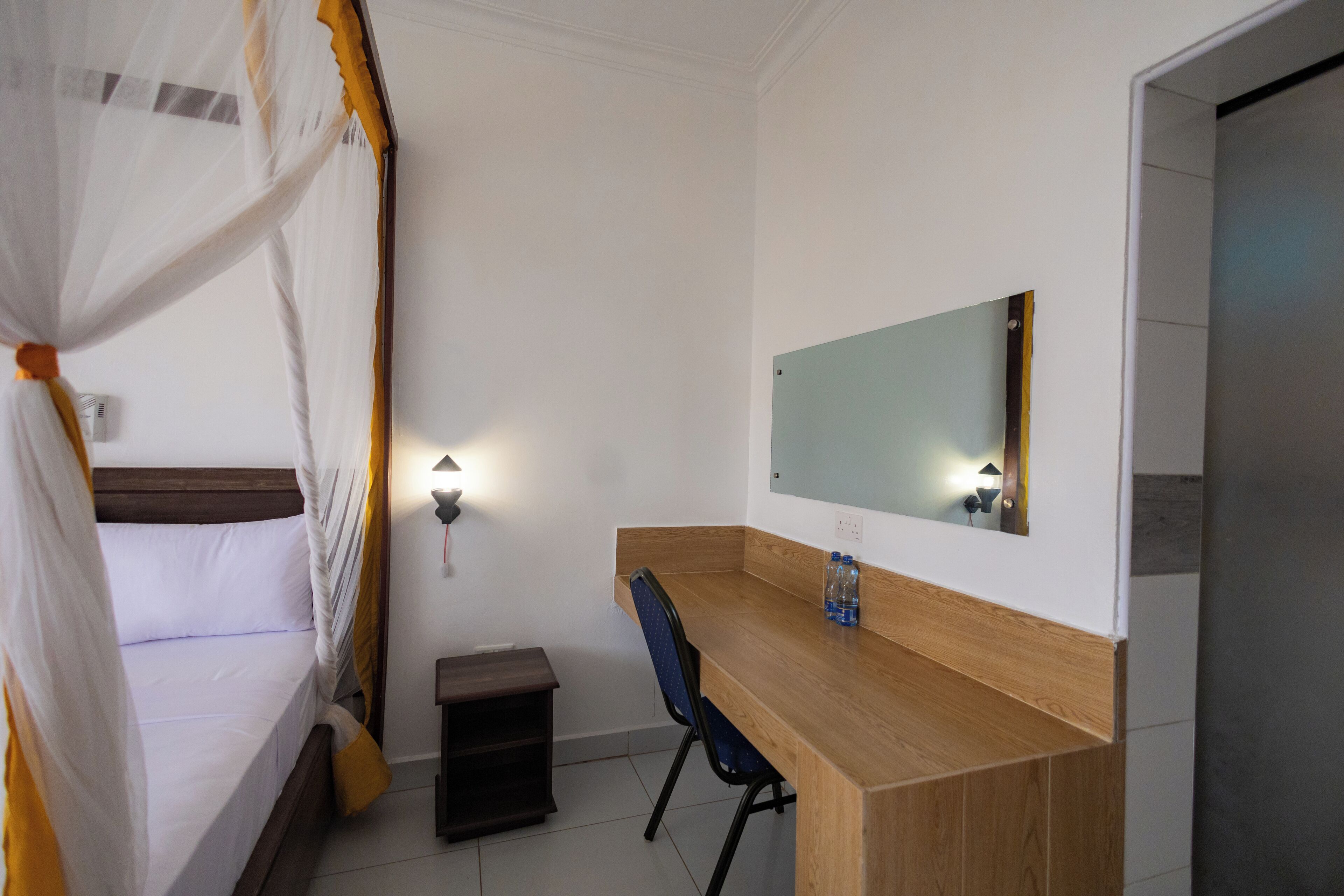 Un dormitorio con cama, escritorio, silla, espejo y mesita de noche.