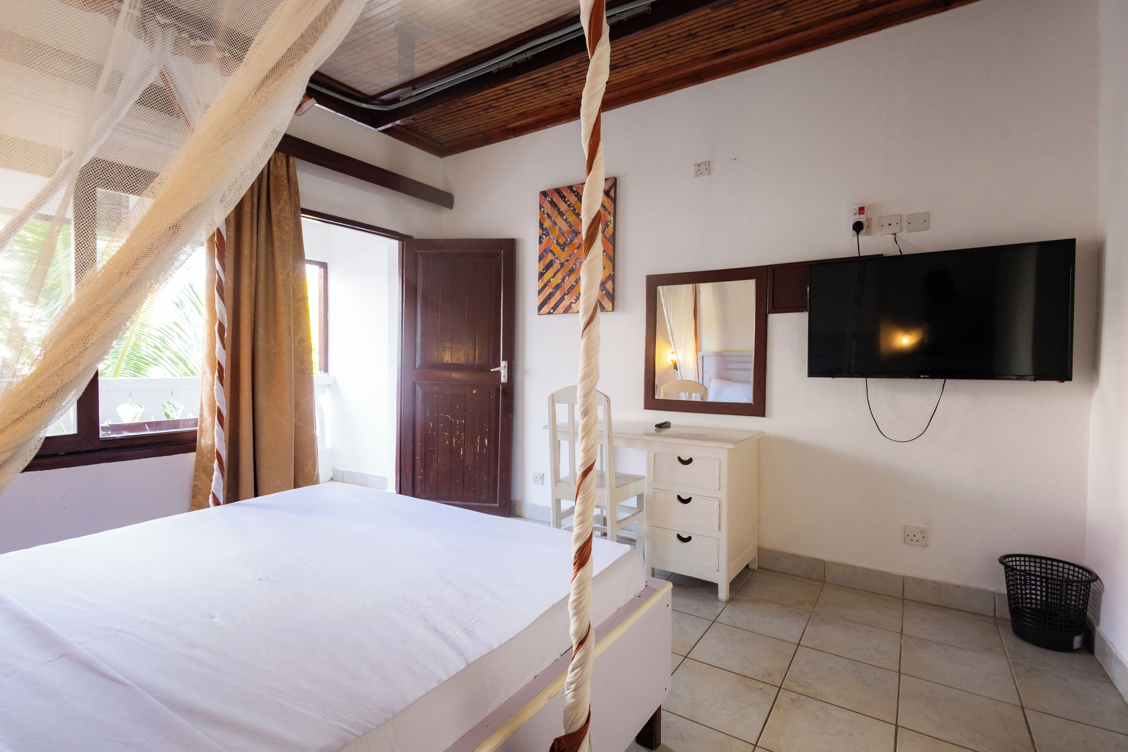 Un dormitorio con una cama, un televisor montado en la pared, un aparador blanco, una silla y una ventana con cortinas.