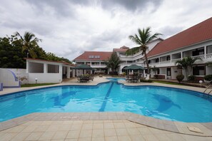 A swimming pool with lounge chairs and umbrellas, surrounded by a building with a red roof and white walls. - The Safiya Hotel (Diani Beach)