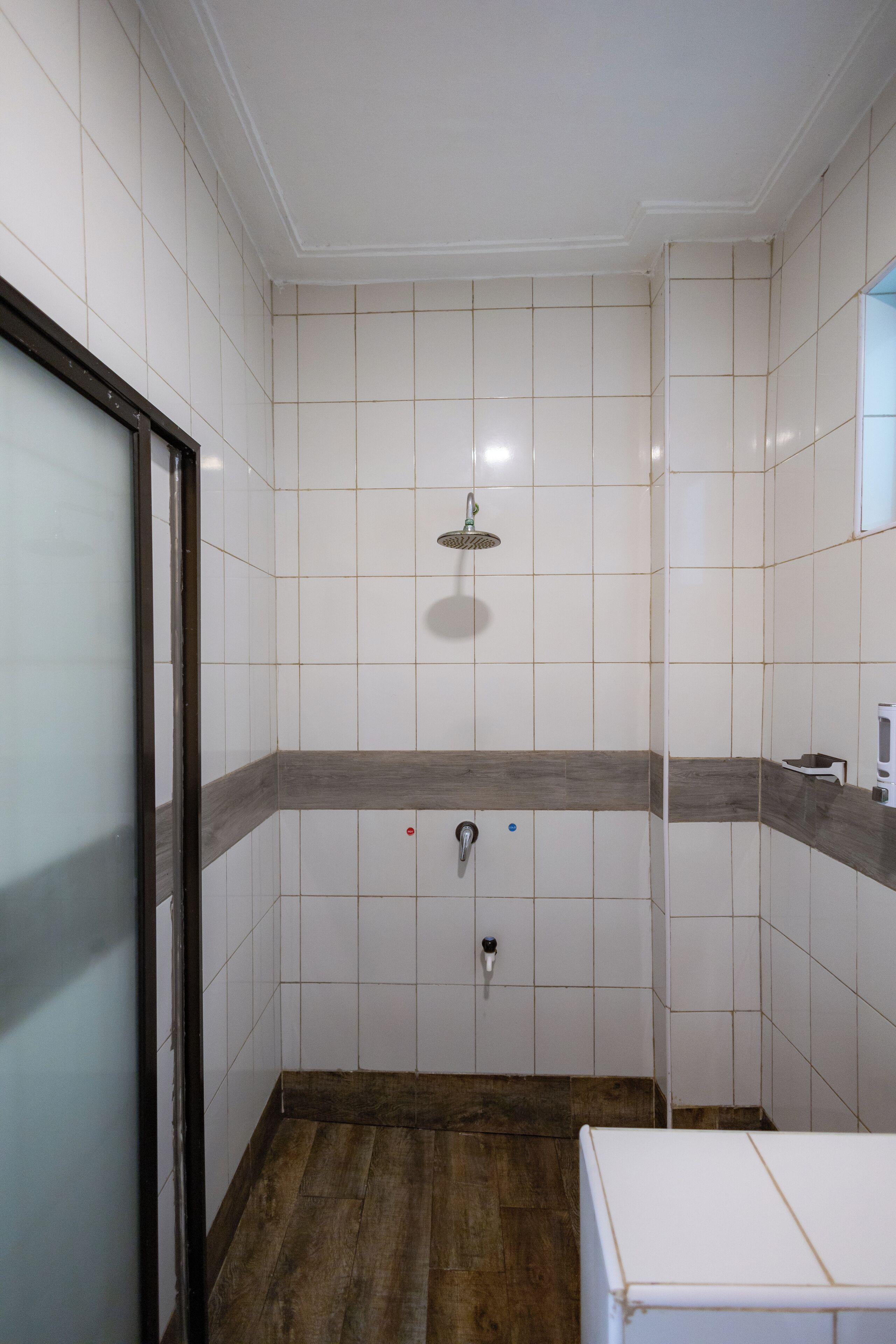 Een badkamer met witte betegelde wanden, een douche en een houten vloer.