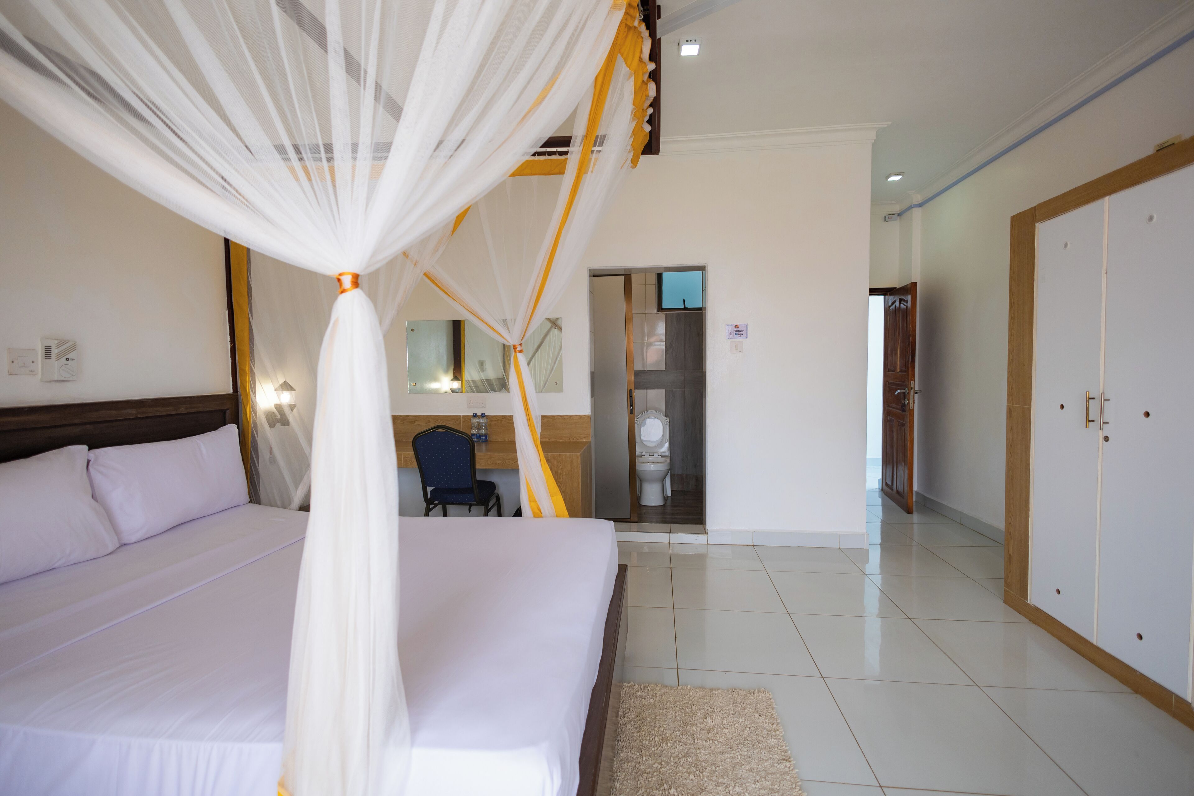 Habitación de hotel con una cama grande, un escritorio y un baño visible a través de una puerta abierta.
