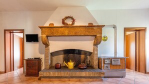 A fireplace with a stone mantle, a television mounted on the wall, and a wooden cabinet to the left. - Achillea Apartment with Shared Pool and Garden (Rosignano Marittimo)