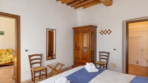 Ein Hotelzimmer mit Bett, Holzschrank, Sesseln, einem kleinen Tisch und einer Dusche.