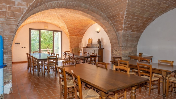 A dining area with a brick arch ceiling, wooden tables and chairs, and a view of greenery outside. - Lavanda Apartment with Shared Pool and Garden (Rosignano Marittimo)