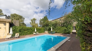 A rectangular swimming pool with a tiled edge, surrounded by a brick patio. There are lounge chairs and umbrellas along the poolside. - Lavanda Apartment with Shared Pool and Garden (Rosignano Marittimo)