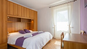 A bedroom with a bed, a wooden wardrobe, a table, and a window with curtains. - Lavanda Apartment with Shared Pool and Garden (Rosignano Marittimo)