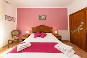 A hotel room with a bed, a chair, a wooden wardrobe, and a picture on the wall.