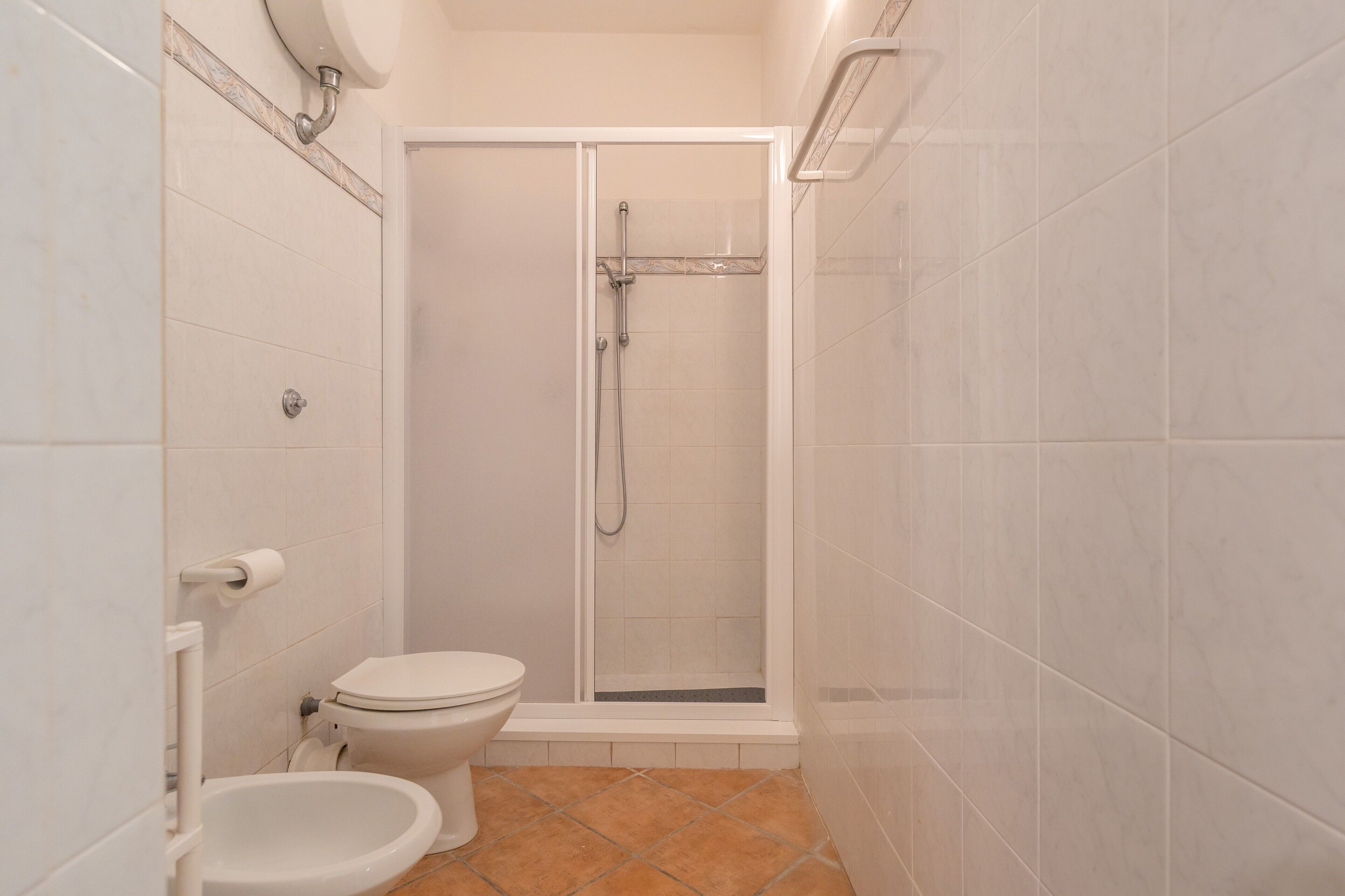 A bathroom with a toilet, a shower enclosure, and a tiled floor.