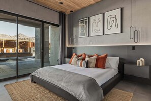 A modern bedroom with a large bed, a sliding glass door to a patio, and abstract wall art.