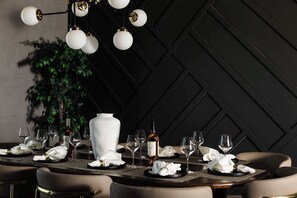 A dining table set with white napkins, wine glasses, and a bottle of wine, with a modern chandelier above.