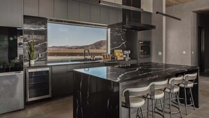 Eine moderne Küche mit einer großen Kochinsel, Barhocker, Blick auf Berge und einer Kaffeemaschine.