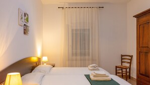 A hotel room with a bed, two bedside lamps, a chair, a wooden wardrobe, and a window with sheer curtains.