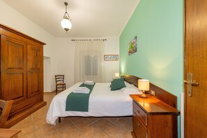 Een hotelkamer met een bed, een houten garderobe, een stoel, een nachtkastje met een lamp en een schilderij aan de muur.