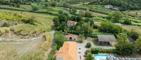A rural property with a swimming pool, a covered outdoor seating area, and a bridge in the background.