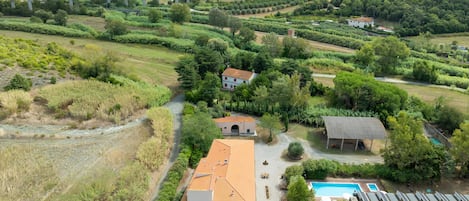 A rural property with a swimming pool, a covered outdoor seating area, and a bridge in the background.