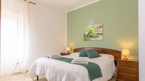 A neatly made bed with white bedding and green pillows, a bedside lamp, and a wall-mounted picture. - Salvia Apartment with Shared Pool and Garden (Rosignano Marittimo)