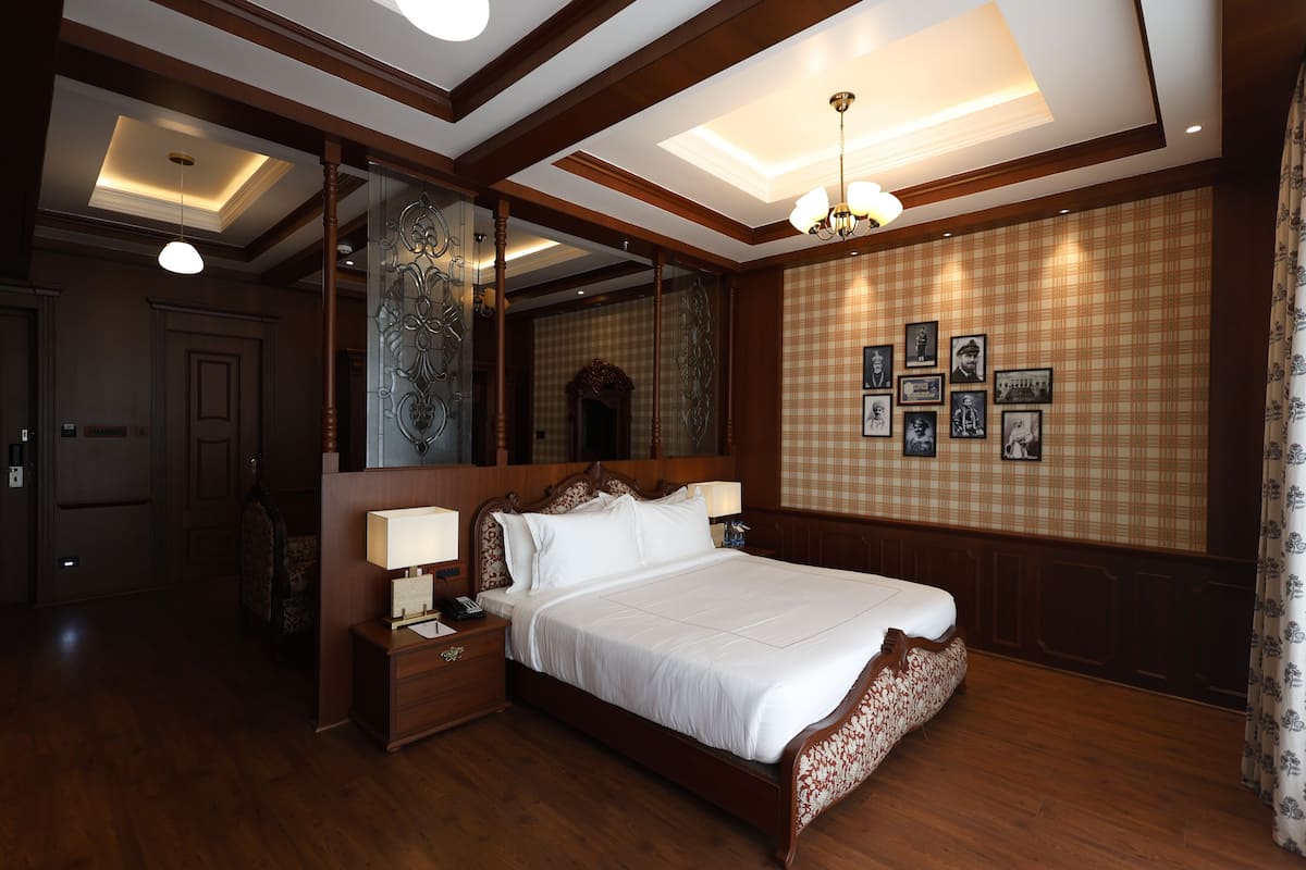 A large, neatly made bed in a hotel room with wooden paneling, a large mirror, and framed pictures on the wall.
