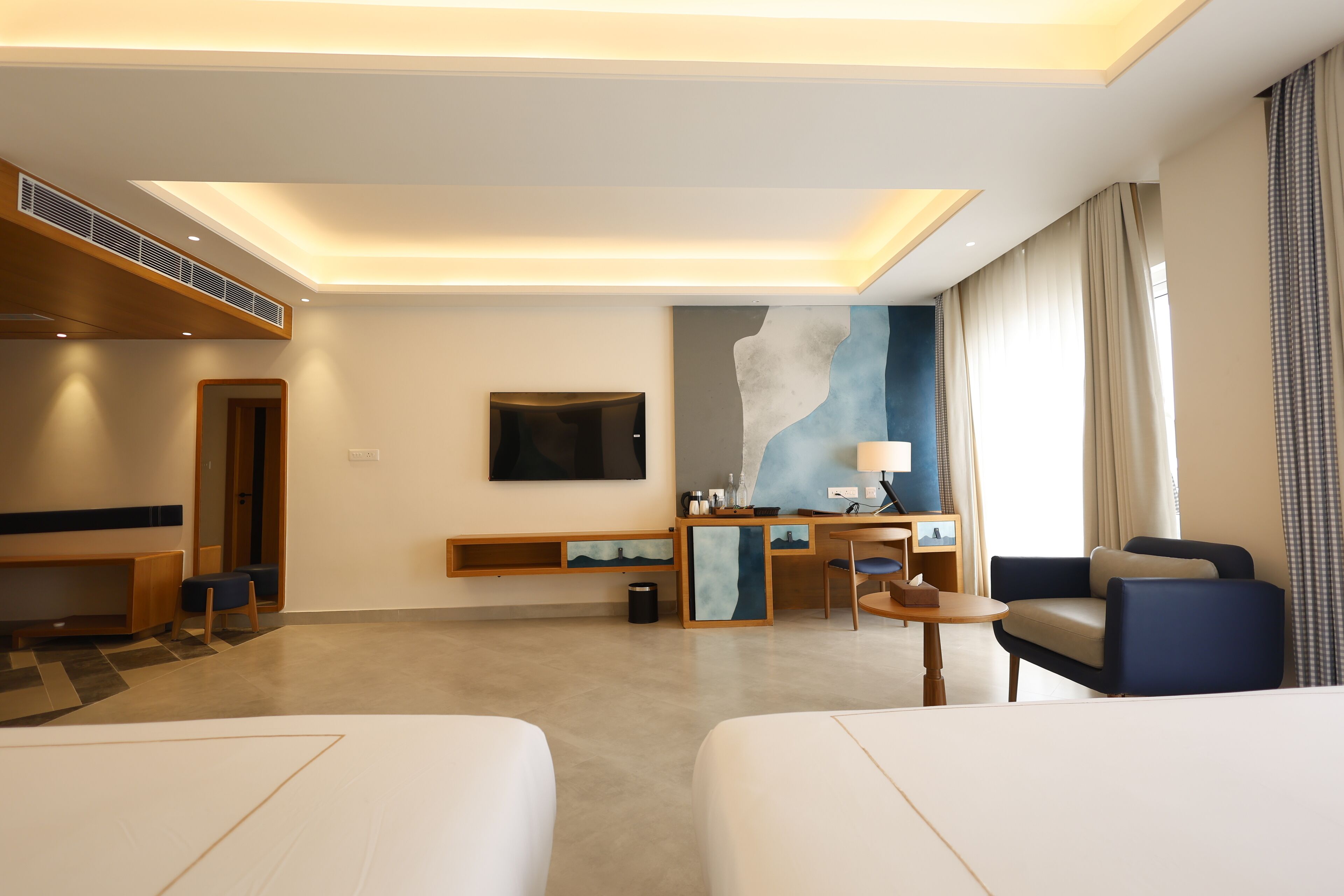 Een moderne hotelkamer met een flatscreen televisie, een bureau met lamp, een stoel en een groot abstract schilderij aan de muur.