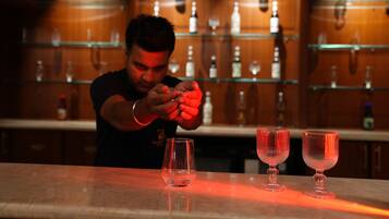 Ein Barkeeper bereitet Getränke an einer Bar zu, im Hintergrund sind Flaschen und Gläser auf Regalen zu sehen.
