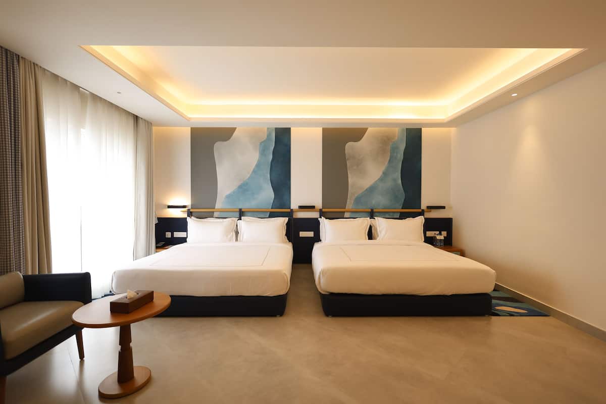 A hotel room with two beds, a sofa, a small table, and abstract wall art.