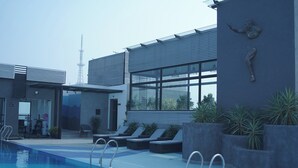 Ein moderner Poolbereich mit Liegestühlen, einem Pool und einem Gebäude mit großen Fenstern und einer Skulptur eines Seehorsches.