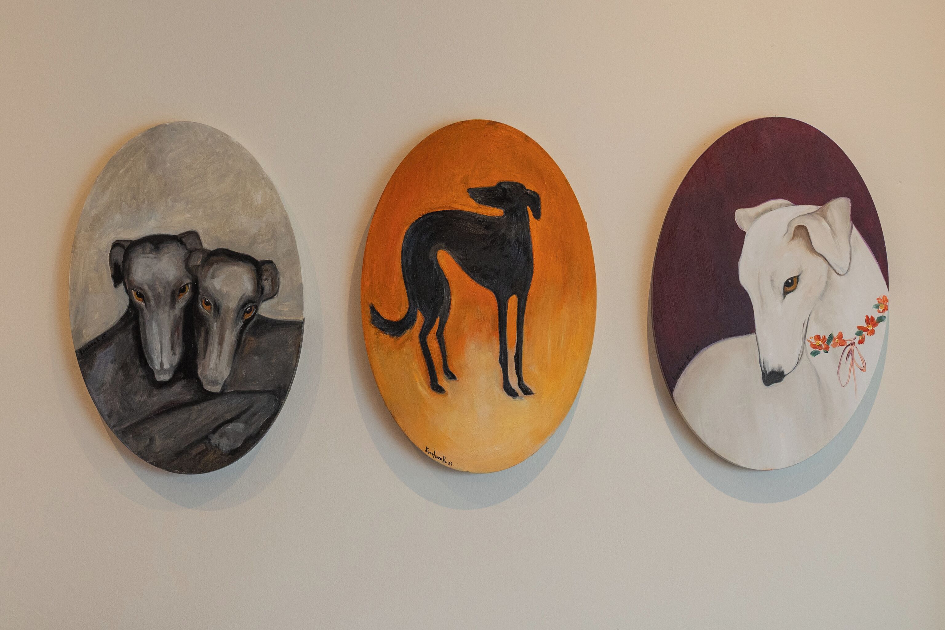 Three oval-shaped paintings of dogs on a wall.
