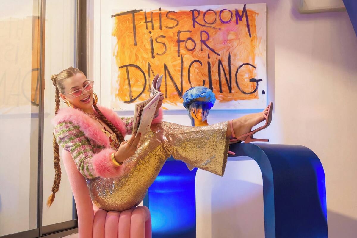 A person sitting on a pink chair in a room with a sign that says 'THIS ROOM IS FOR DANCING.'