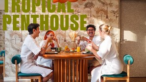 A group of people seated around a wooden table in a room with a tropical-themed wallpaper and a large sign reading 'TROPICAL PENTHOUSE'. - 5loft Anti-Hotel, Silom, Bangkok (Bangkok)