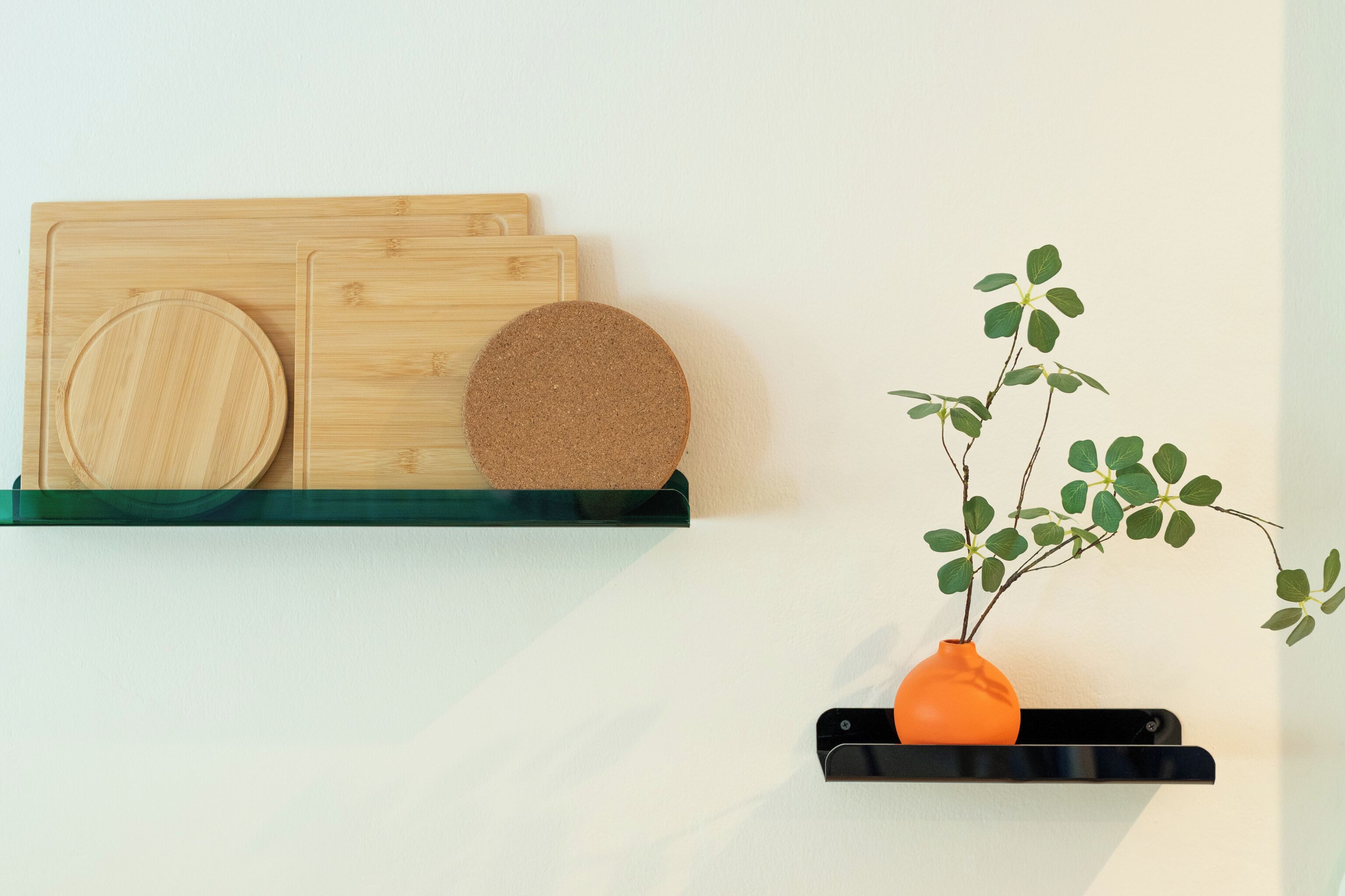 A kitchen with wooden cutting boards and a cork board on a green shelf, and a potted plant on a black shelf.