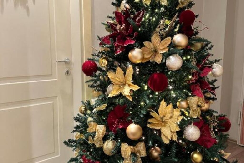 Un sapin de Noël décoré d’ornements dorés et rouges, placé dans une pièce dont la porte est blanche.