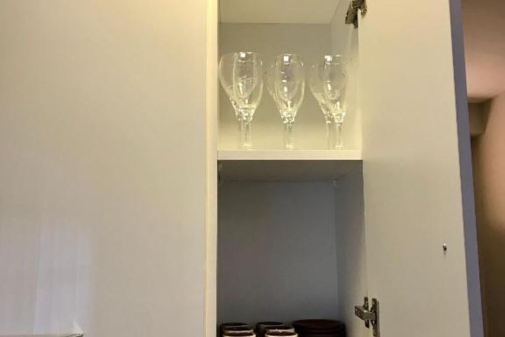 A room with a white wall and a door. There is a shelf with three clear glasses on it.