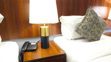 Habitación de hotel con cabecera de madera, una mesita de noche con lámpara, teléfono y almohadón decorativo.