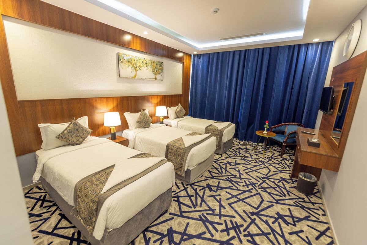 A hotel room with two beds, a desk, a chair, a small table, and a large window with curtains.