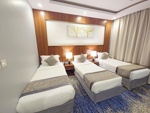 A hotel room with three beds, a wooden headboard, a painting, and a blue carpet. - Romance Room hotel (Makkah)