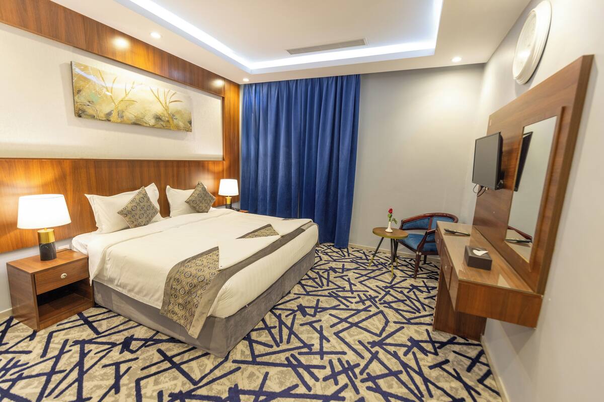 A hotel room with a large bed, bedside tables with lamps, a small desk with a mirror, and a blue curtain.