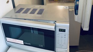 Een magnetron op een aanrecht, een koelkast met vriesvak en een plank met diverse etenswaren.
