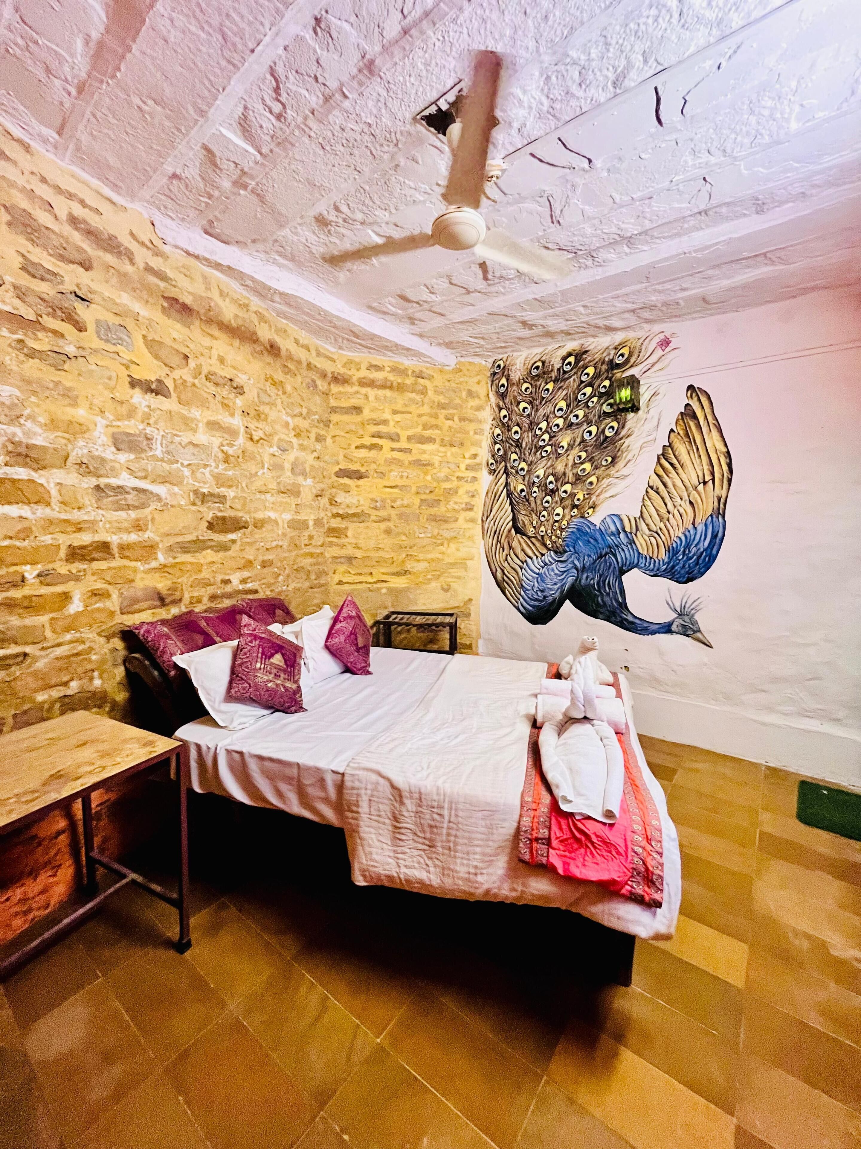 Una habitación con pared de piedra, una cama con almohadas, una mesita de noche de madera y un ventilador de techo.